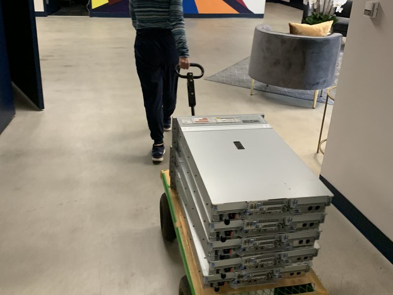 A hand truck stacked with finished rack servers being wheeled down a hallway.